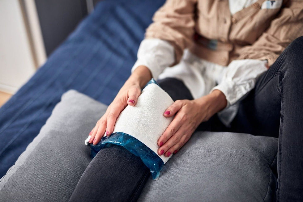 Hands applying an ice pack wrapped in a towel on a knee, with dark jeans and a blue bedspread in the background, conveying rest.