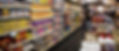 Grocery aisle filled with colorful cereal and snack boxes. Shoppers browse in a well-lit store, with visible sale signs, creating a bustling mood.