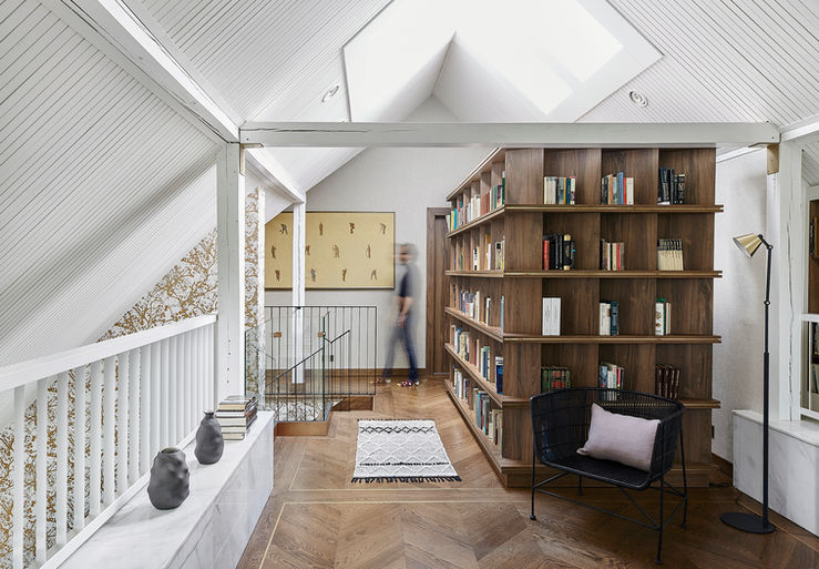 Loft library with pitched ceiling, skylight, parquet wood floor, wood library, books, exposed structural beams.