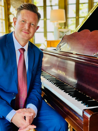 Pianist seated at grand piano in blue suit inside Boettcher Mansion