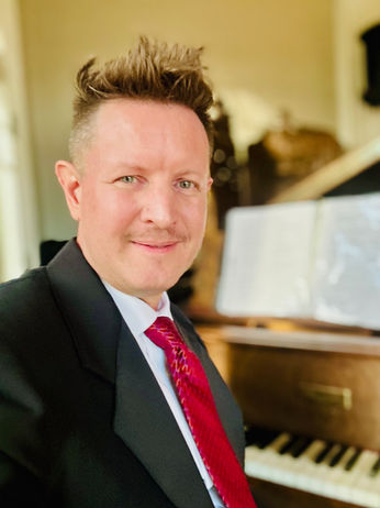 Portrait of pianist Tanner Palmer at the Grant-Humphreys Mansion wearing a navy suit and red tie in the mansion’s music room
