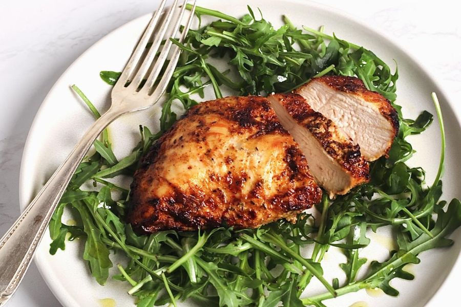 Grilled chicken on a bed of fresh arugula on a white plate with a silver fork; appetizing and neatly presented.