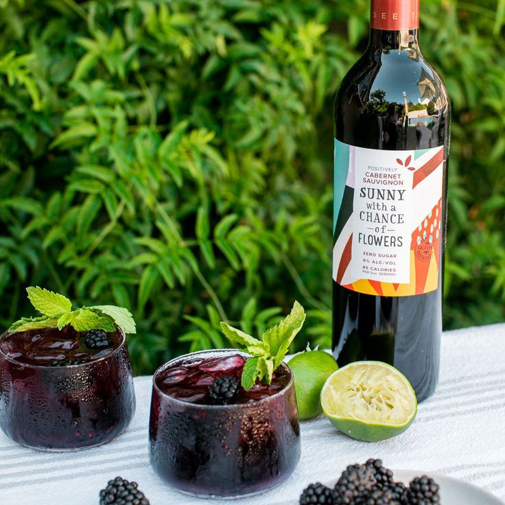 Refreshing glasses of Cabernet Sauvignon enhanced with a squeeze of lemon and garnished with fresh blackberries, accompanied by a vibrant bottle of wine on a sunny day.