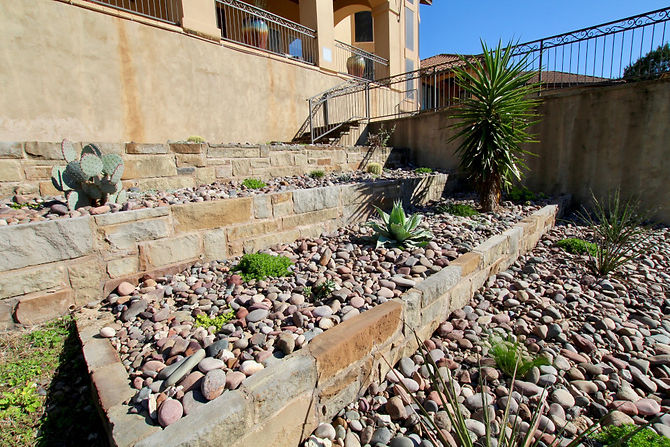 This client came to us wanting to add plants to their beds. When the wife mentioned that she hated the limestone cliff in their front yard, we decided the best thing to do would be to build up the cliff and add beds above it. We constructed a limestone wall with boulders, incorporating several cubbies to add plants. Down the wall, we also added various varieties of plants to spread across the bed along with some large yuccas, trees and succulents.