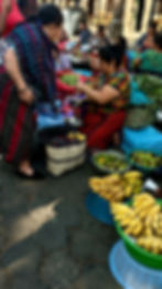 Two women in colorful traditional clothing at the market with bananas, green beans and all types of fruits and vegetables.