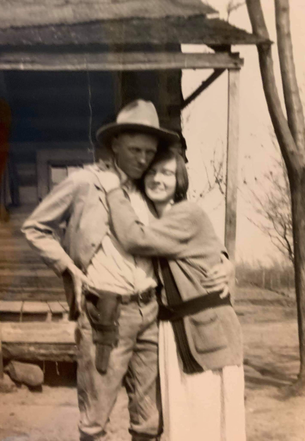 Historic photo of loving couple on East Texas farm. Man has sidearm in holster. Woman hugging man at old farmhouse.