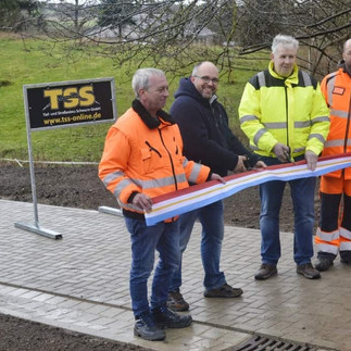 Vier Männer in Warnwesten bei der Eröffnung eines gepflasterten Weges. Im Hintergrund Wiese und ein Schild der Firma TSS Schwerin.