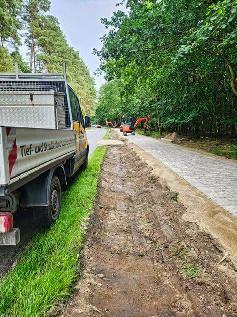 Radwegbau im Wald: Firmentransporter der Firma TSS am Straßenrand, Bagger und frischer Erdstreifen neben neuem Weg.
