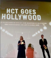 Zwei Personen in Abendkleidung stehen auf einer Bühne. Im Hintergrund leuchtet der Text "HCT GOES HOLLYWOOD".