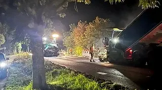 Asphaltierarbeiten in der Nacht mit zwei Asphaltiermaschinen unter Bäumen mit hellen Scheinwerfern.