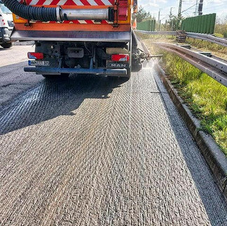 Eine orangene Straßenkehrmaschine reinigt eine abgefräste Fahrbahn, rechts Leitplanken und dazwischen grüne Wiese.