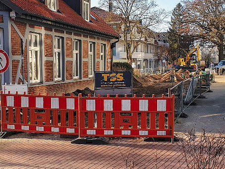 Baustelle vor Fachwerkhaus, orange-weiße Absperrung, gelber Bagger im Hintergrund. Schild mit Aufschrift TSS.