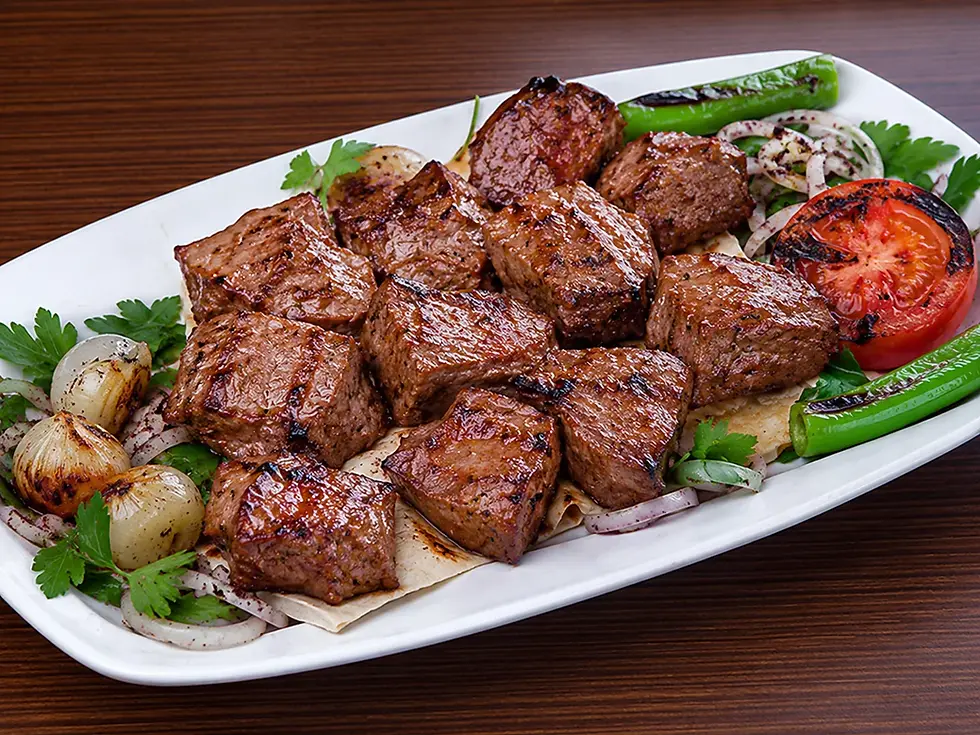 Assiette de viande grillée avec poivrons, tomate, oignons et persil, servie sur une table en bois.