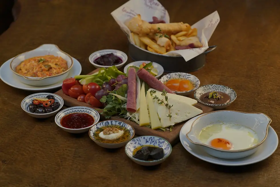 Un copieux petit-déjeuner/mezzé présenté sur une table en bois : fromage, raisins, tomates, olives, sauces, plats frits et œufs.