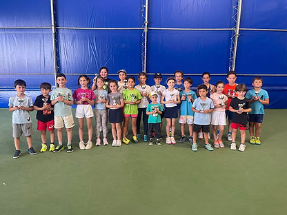 A group of tennis kids holding trophies on a tennis court