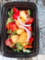 A vibrant salad with red peppers, golden beets, tomatoes, red onion rings, and pomegranate seeds in a black meal prep contain