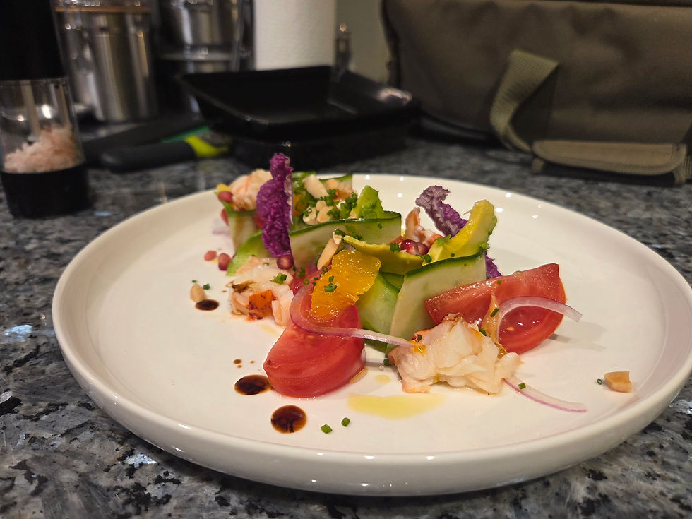A white plate holds a plated lobster salad with cucumber, avocado slices, tomato wedges, and purple cauliflower florets.