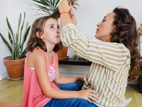 Mother examining her young daughter's hair and scalp for head lice at home.