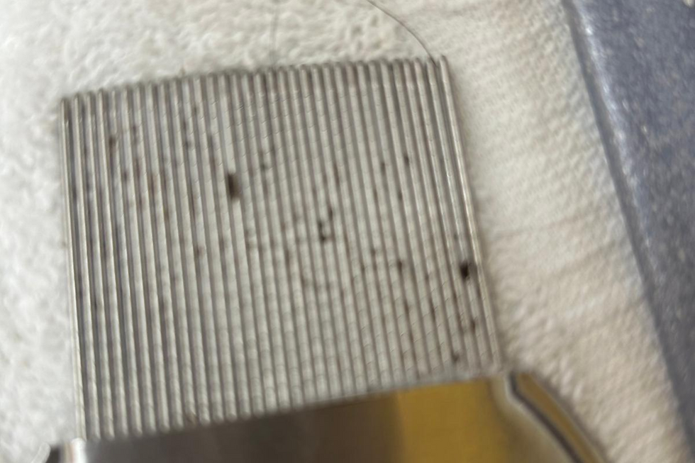 Close-up view of a fine-toothed metal lice comb with tiny caught debris resting on a white towel.