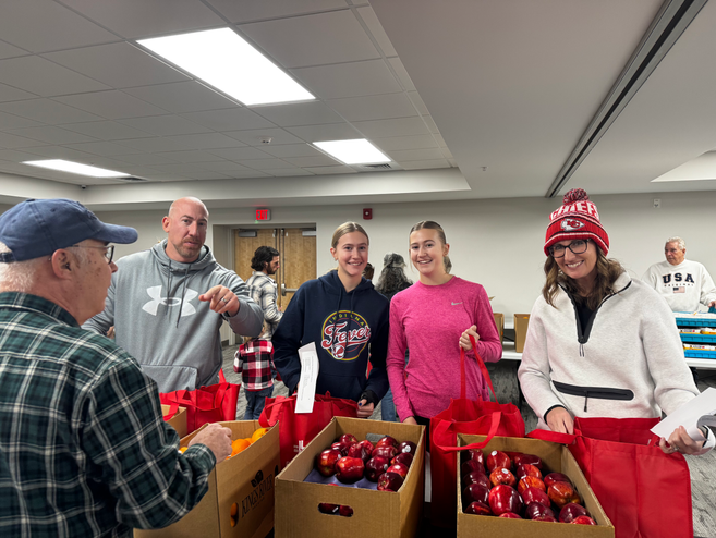 Four Volunteers packing Christmas Food Baskets, smiling at the camera