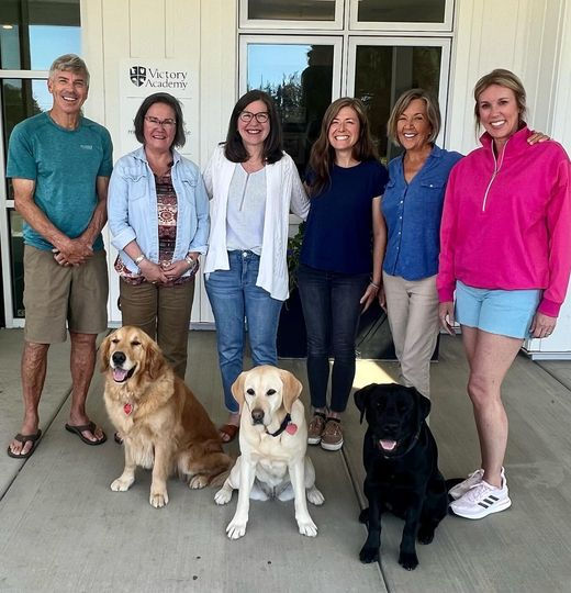 A group of people stand smiling behind 3 dogs.