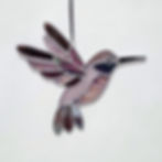 Handmade stained glass hummingbird in flight with iridescent shifting colors and a sparkling dichroic glass eye, hanging in a