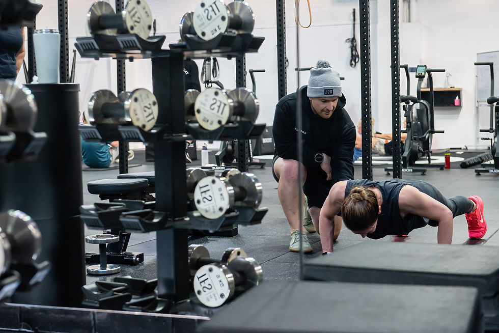 Woman doing push-ups; trainer assisting in a gym setting with weights.