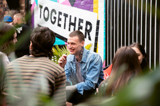 candid photograph of a man sat at an event or party outdoors, smiling