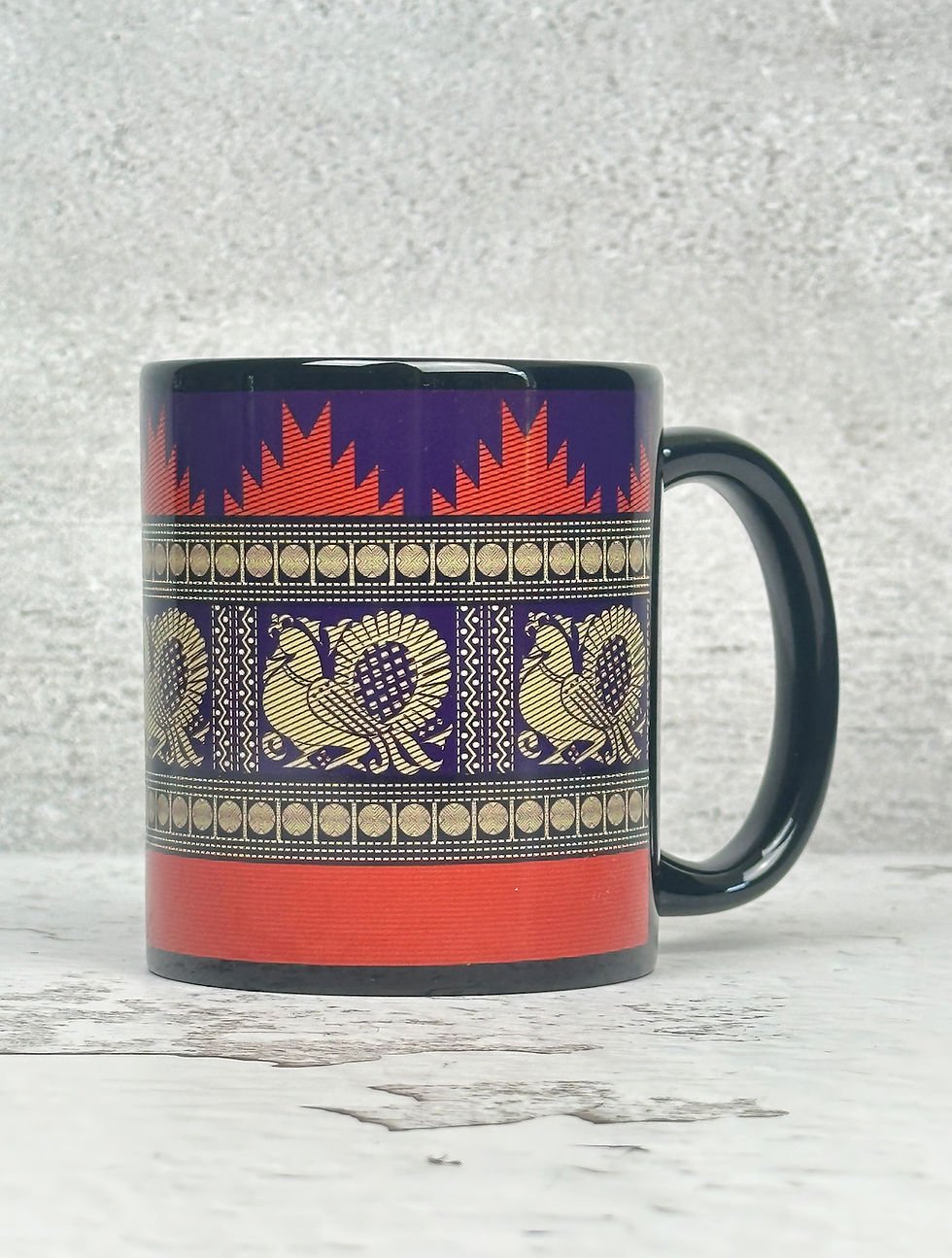 Black ceramic mug with South Indian-inspired peacock and gopuram (temple) border design in purple and rust orange