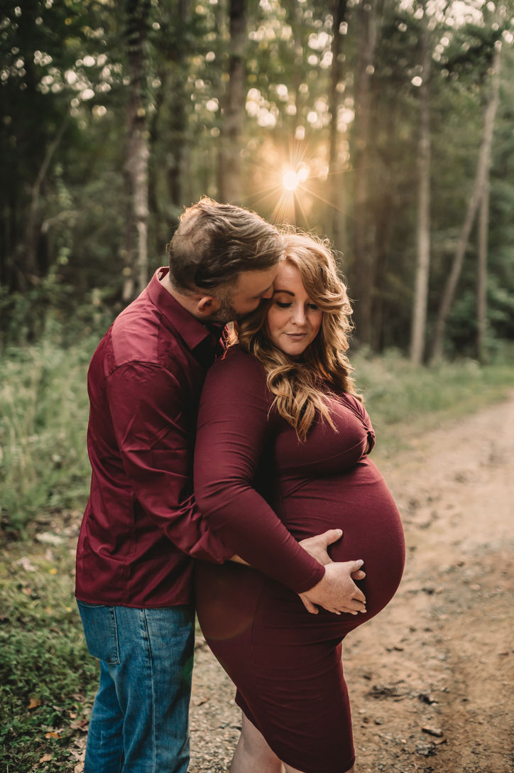 Pregnant woman getting hugged by her husband during a maternity photoshoot in Latta Nature Preserve. 