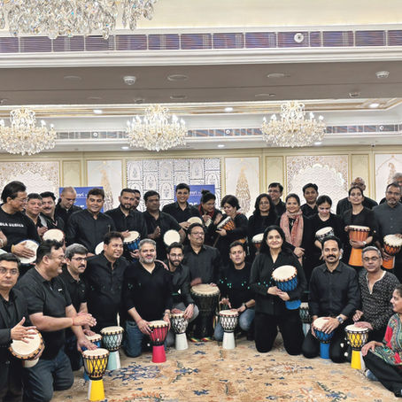 Employees from different departments participating in a drum circle workshop, collaborating through rhythm to improve communication, teamwork, leadership development, employee engagement, and workplace culture.