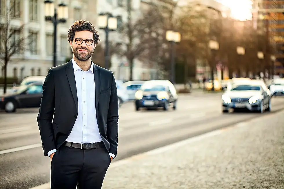 Businessportrait eines lächelnden Mannes im Anzug in Berlin, aufgenommen vor einer belebten Straße mit städtischem Verkehr – professionell von Concept Photography Berlin.