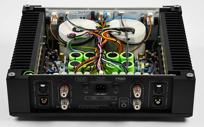 Open amplifier showing complex wiring, green capacitors, and labeled inputs. Black exterior with visible text. Technical and detailed.