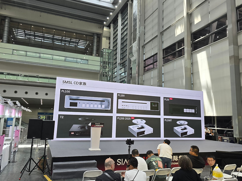 Stage with product display, "SMSL CD" models shown on screen. People seated in front, large modern building interior in background.