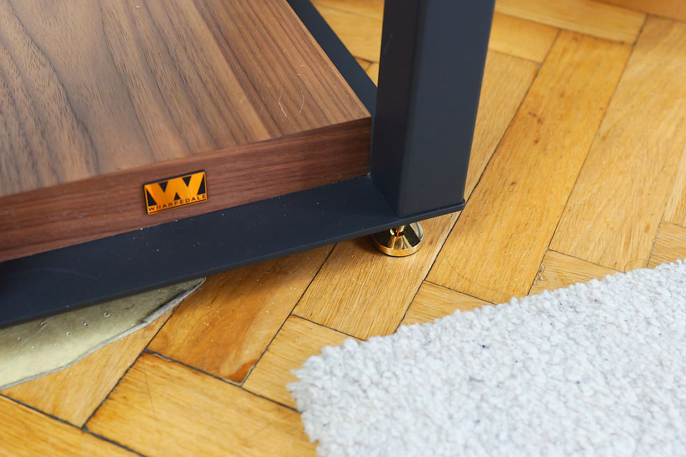 Wooden speaker stand with a "Wharfedale" logo on hardwood floor, featuring a metal base and brass foot. A white rug partially visible.