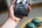 Hand holds a phone playing "Swan (Remastered)" by Scott Walker. Green headphones in the blurred background. Screen shows playback controls.