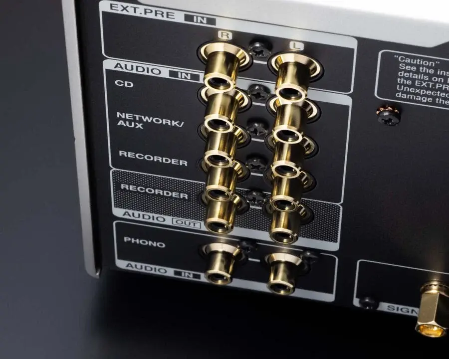 Close-up of an audio equipment panel with multiple gold RCA inputs and outputs labeled for various functions like CD and network/aux.