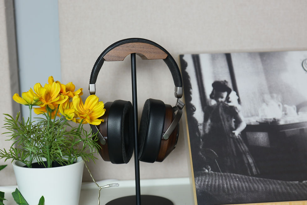 Headphones on a stand with a wood accent next to a potted plant with yellow flowers. A black-and-white vintage photo is in the background.