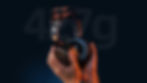 Hands holding sleek black headphones, lit with orange and blue hues, against dark background with "427g" text. Futuristic and tech-focused.