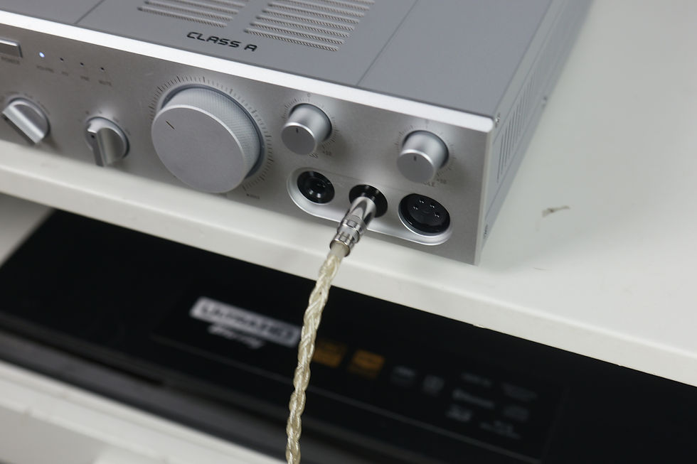 Silver Class A audio amplifier with knobs and a braided cable plugged in on a white shelf.