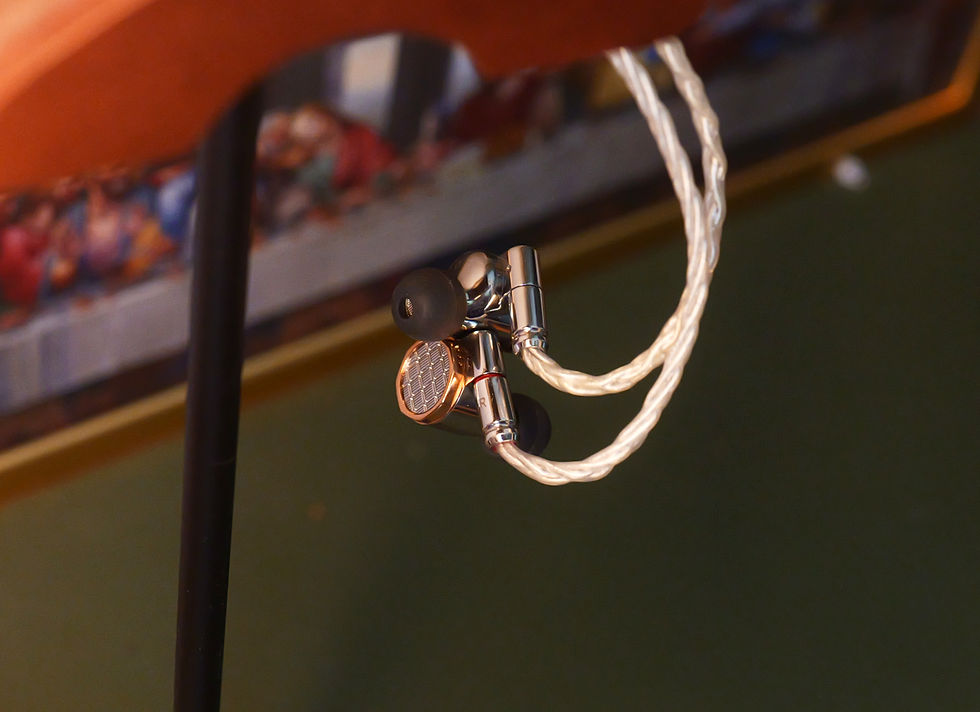 Close-up of silver wired earbuds hanging from a stand, with a blurred indoor background and warm orange tones.