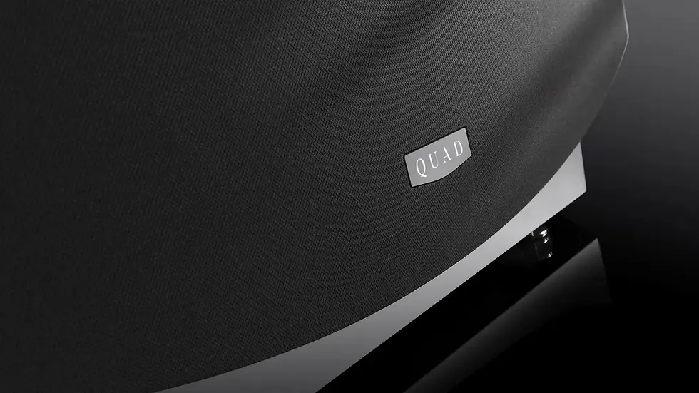 Close-up of a black speaker with the label "QUAD" on a sleek black surface. Reflective and minimalistic design.