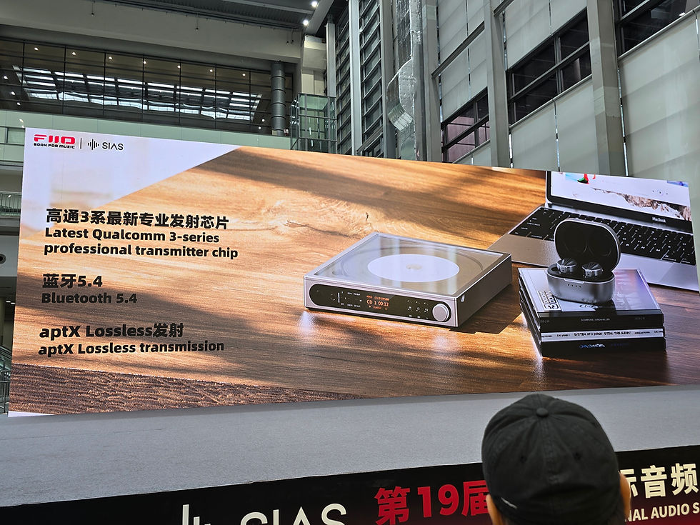 Advertisement banner in a modern building showing a laptop, earbuds, and a CD player. Text highlights Qualcomm chip, Bluetooth 5.4, aptX Lossless.