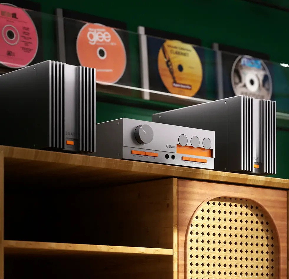 Silver audio equipment with orange accents on a wooden shelf. CDs displayed on a green wall above, featuring varied colors and designs.