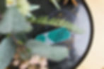 A teal USB drive with geometric patterns rests on a black marbled surface, partially obscured by green and pink foliage in the foreground.