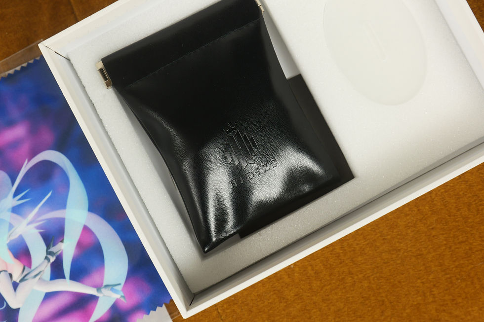 Black leather HIDIZS pouch in a white foam-lined box, with a colorful insert partially visible on the left.