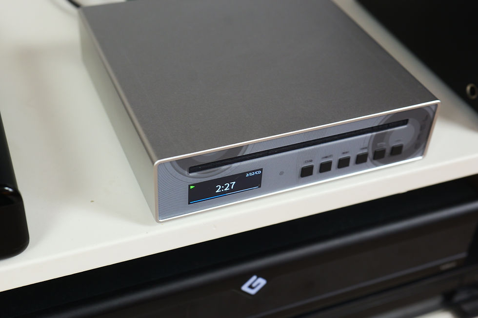 Silver CD player on a white shelf displaying 2:27 on a digital screen. Black buttons and slot visible, with minimal background detail.