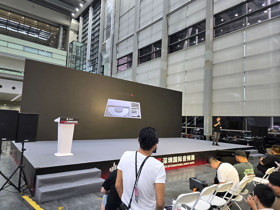 A speaker on stage presents "Concept R" at an indoor event. Attendees are seated in rows. Large screen and podium visible. Text in Chinese.