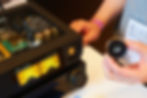 Hands hold a round -20.0 display beside an open Luxsin audio amplifier with glowing VU meters on a table.