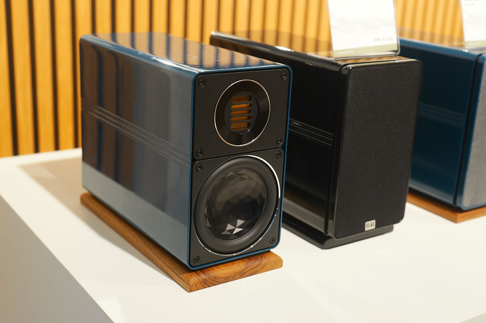 Three modern blue-and-black speakers on wooden bases displayed on a white table, with ELAC logo visible on the front speaker.